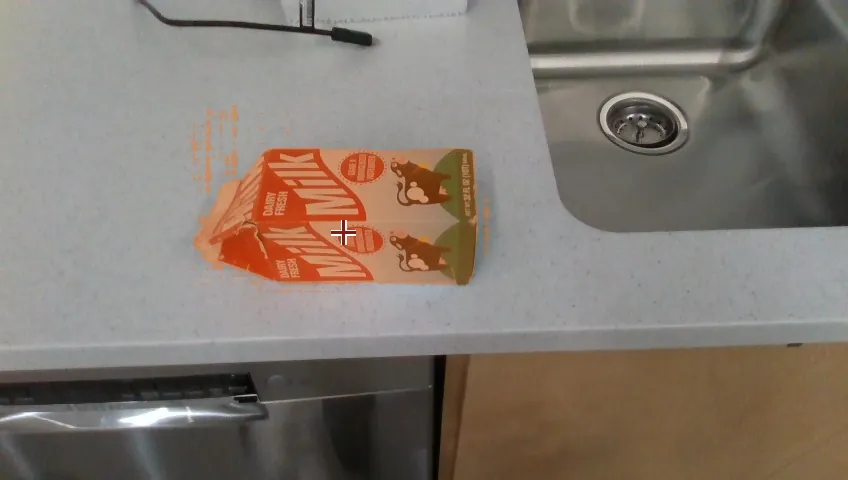 Ego view: a milk carton on the counter highlighted with an orange mask and a crosshair on its top face, the point selected by the VLM