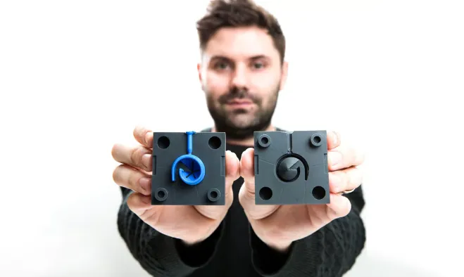 一位工程师双手展示两块树脂 3D 打印的功能件